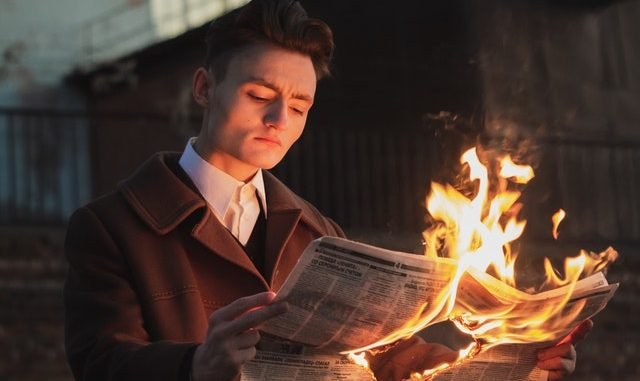 man reading burning newspaper